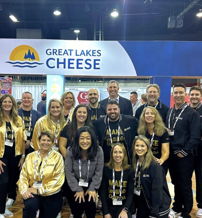 Group in coordinated attire at "Great Lakes Cheese" booth, exuding joy and teamwork at a lively trade show event.