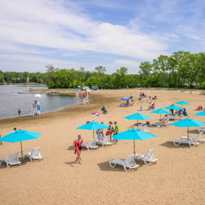 Bright beach scene with turquoise umbrellas, lounge chairs, and people enjoying sunbathing, swimming, and socializing.