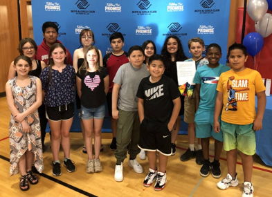 A joyful group of diverse kids and teens smiles in a gym, celebrating together under a blue backdrop with balloons.