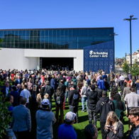 A lively crowd gathers outside a modern arts venue on a sunny day, filled with excitement, joy, and community anticipation.