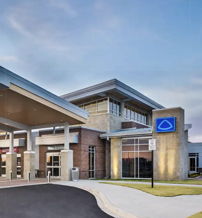Modern healthcare building with sleek lines, inviting entrance, and a serene sunset sky, evoking comfort and hope.