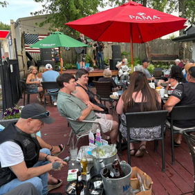Outdoor gathering on a wooden deck with lively conversations, food, drinks, and live entertainment, evoking joy and camaraderie.