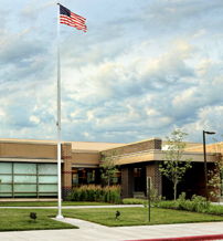 A modern school building with a flagpole, neat landscaping, and a cloudy sky evokes community, patriotism, and a nurturing environment.