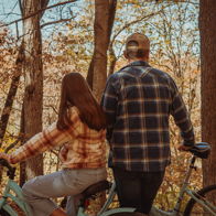Two individuals in cozy attire stand by bicycles in a forest with autumn leaves, radiating warmth and tranquility.