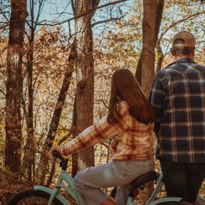 Two individuals in cozy attire stand by bicycles in a forest with autumn leaves, radiating warmth and tranquility.