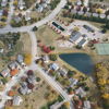 Aerial view of a suburban neighborhood with houses, winding roads, autumn foliage, a serene pond, and tennis courts.