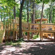 Wooden playground in lush greenery, featuring climbing areas and ramps, evoking joy, adventure, and a connection to nature.