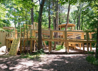 Wooden playground in lush greenery, featuring climbing areas and ramps, evoking joy, adventure, and a connection to nature.