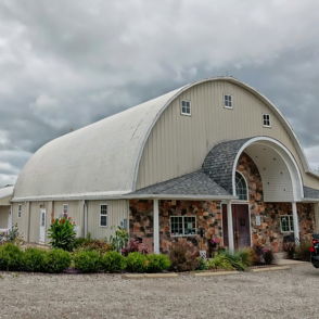 A barn-like building with a curved roof and silos amidst greenery, exuding rustic charm under an overcast sky.