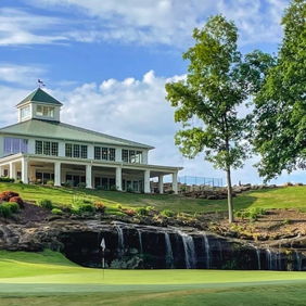 A serene golf course with lush grass, a charming clubhouse, tall trees, and a small waterfall under a clear blue sky.