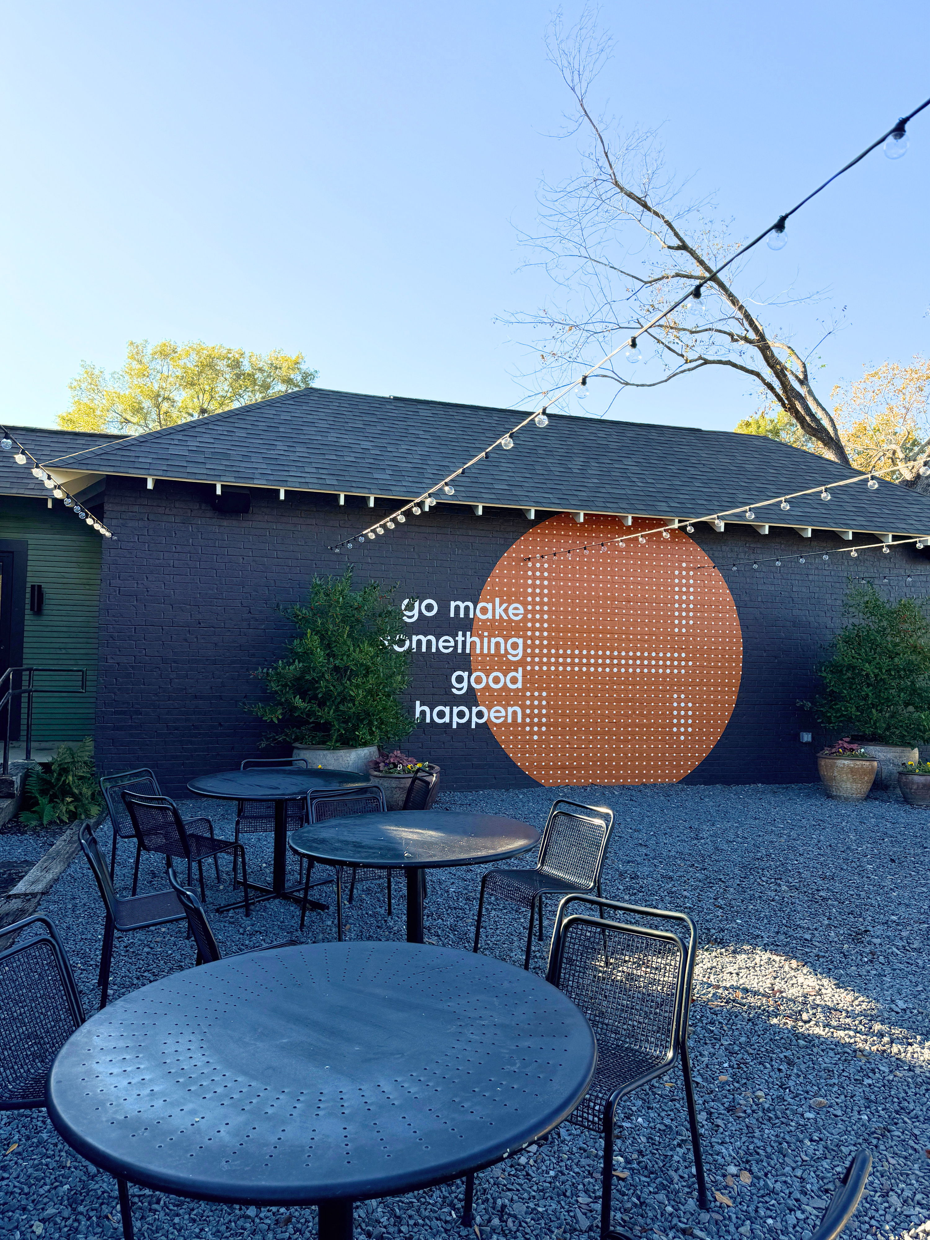 Outdoor space with round tables, black chairs, and an inspiring mural featuring an orange circle and the phrase "go make something good happen."