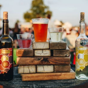 Cheerful outdoor gathering with wine, colorful drinks, and beer on wooden blocks, evoking relaxation and camaraderie.