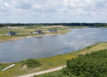 Serene landscape with calm water, lush greenery, scattered houses, and a bright sky, evoking peace and tranquility.