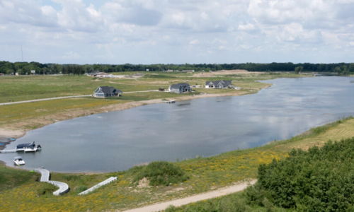 Serene landscape with calm water, lush greenery, scattered houses, and a bright sky, evoking peace and tranquility.