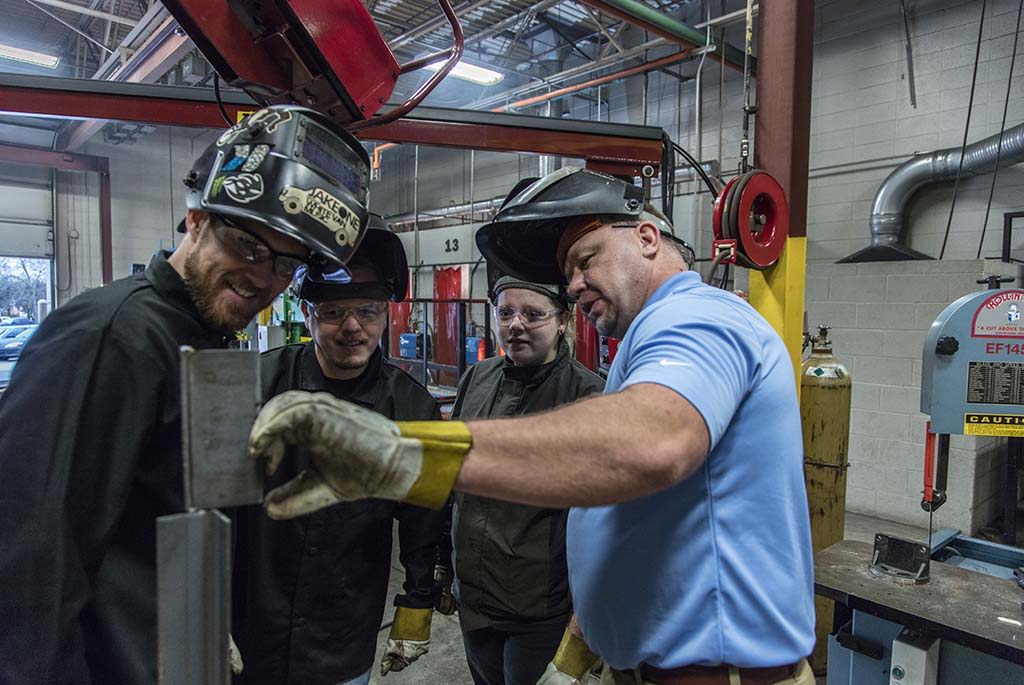 Individuals in a workshop engage in welding, focusing on learning and teamwork while practicing safety precautions.