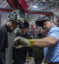 Individuals in a workshop engage in welding, focusing on learning and teamwork while practicing safety precautions.