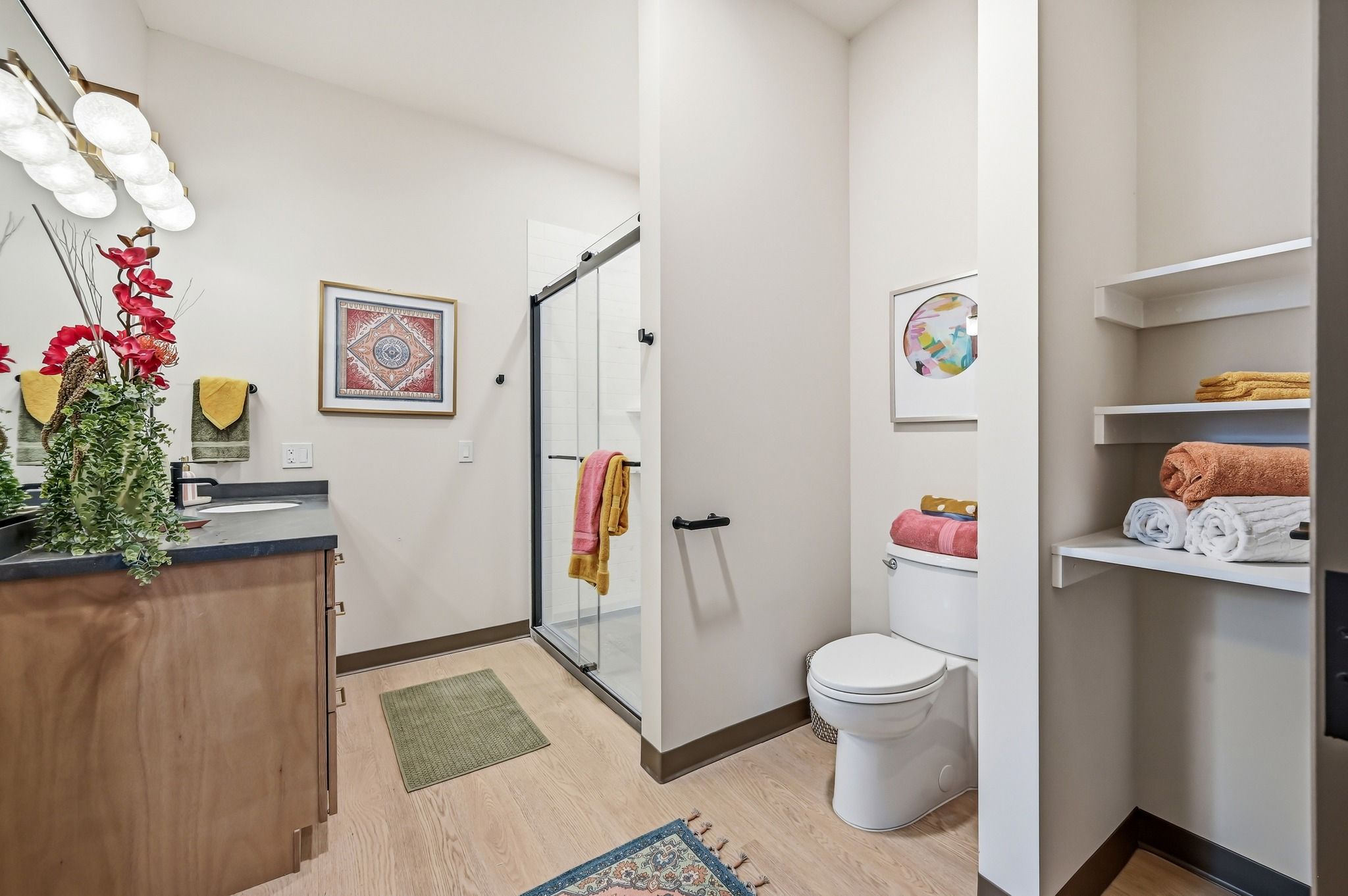 Modern bathroom with clean lines, wooden vanity, glass shower, colorful decor, and bright lighting for a cheerful atmosphere.