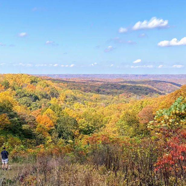 Autumn landscape with vibrant foliage, blue sky, and two individuals enjoying the tranquil beauty of nature.