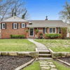 Charming brick house with a stone pathway, lush lawn, and flower beds, evoking warmth and nostalgia in a serene suburban setting.