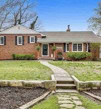 Charming brick house with a stone pathway, lush lawn, and flower beds, evoking warmth and nostalgia in a serene suburban setting.