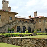 A grand stone mansion with arched windows, chimneys, and a lush garden, evoking elegance and a sense of history.