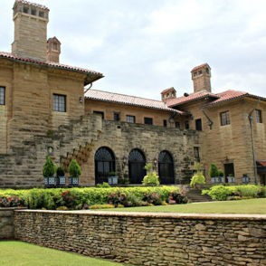 A grand stone mansion with arched windows, chimneys, and a lush garden, evoking elegance and a sense of history.