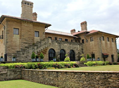 A grand stone mansion with arched windows, chimneys, and a lush garden, evoking elegance and a sense of history.