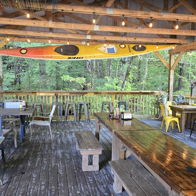 Outdoor seating area under wooden structure, with cozy decor and greenery, invites relaxation and social gatherings in nature.