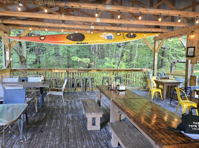 Outdoor seating area under wooden structure, with cozy decor and greenery, invites relaxation and social gatherings in nature.