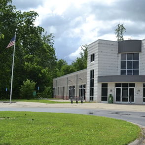 Modern YMCA building in a green area, with grassy space, pathway, and American flag, exuding community and wellness.