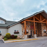 Cozy lodge with rustic wood and stone design, welcoming entrance, and charming landscaping evokes warmth and tranquility.
