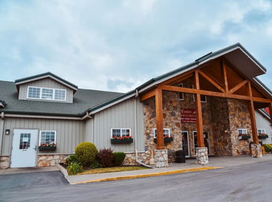 Cozy lodge with rustic wood and stone design, welcoming entrance, and charming landscaping evokes warmth and tranquility.