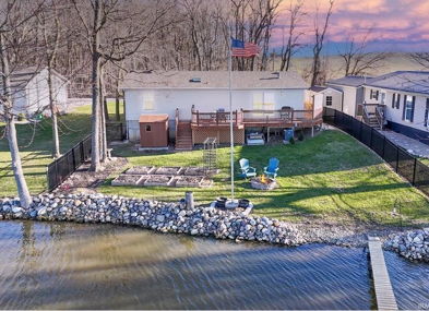 A tranquil lakeside scene features a cozy house, dock, and lounge chairs, surrounded by trees and a flagpole with an American flag.