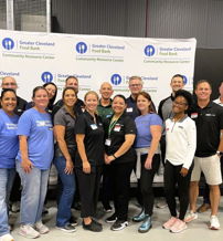 A smiling group stands in front of a food bank logo, embodying community spirit and teamwork at a volunteer event.