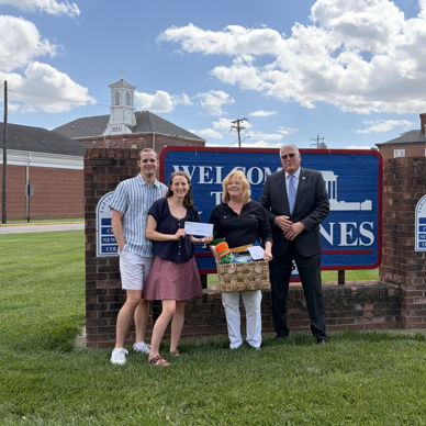Four smiling individuals hold a basket and cards in an outdoor setting, evoking joy and community spirit.