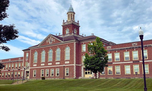 A large brick school with a clock tower, large windows, and a well-kept lawn, evoking nostalgia and a sense of community.
