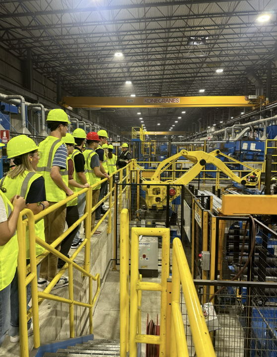 A group in safety gear tours a manufacturing facility, evoking curiosity, safety, teamwork, and professionalism.