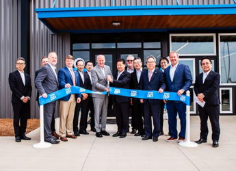 Group in formal attire at a celebratory ribbon-cutting event, holding a large blue ribbon, radiating positivity and success.