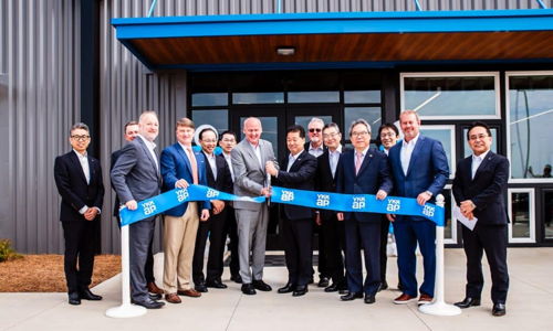 Group in formal attire at a celebratory ribbon-cutting event, holding a large blue ribbon, radiating positivity and success.