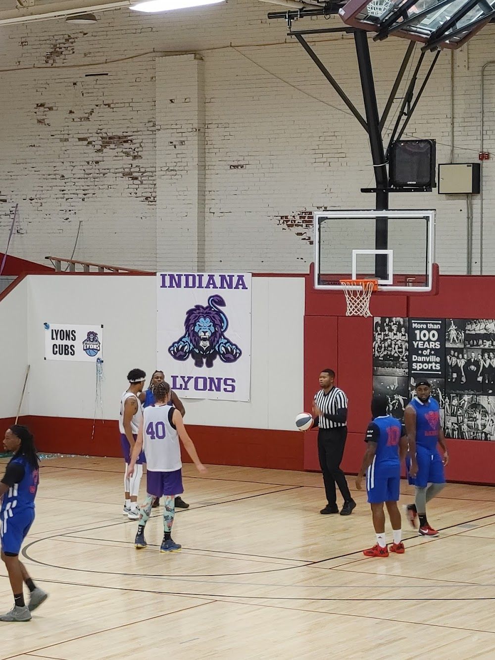 A dynamic basketball game in a gym; players in blue, white, and purple uniforms with a referee overseeing the action.