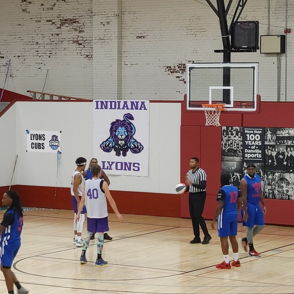 A dynamic basketball game in a gym; players in blue, white, and purple uniforms with a referee overseeing the action.