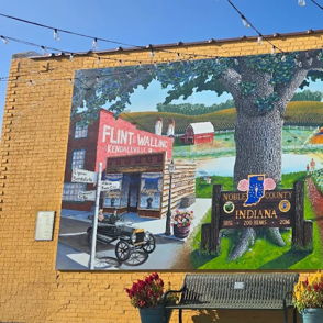 Vibrant mural on yellow wall depicts a lively community scene, evoking joy, nostalgia, and a sense of belonging.