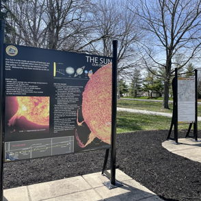 Outdoor exhibit with two panels on solar science, surrounded by trees and blue sky, promoting learning and curiosity.