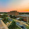 Sunset view of a hospital with vibrant skies, trees, and parked cars, evoking calmness, hope, and a sense of care.