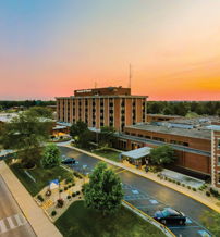 Sunset view of a hospital with vibrant skies, trees, and parked cars, evoking calmness, hope, and a sense of care.
