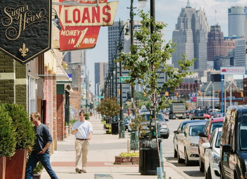 Bustling urban scene with shops, pedestrians, and modern skyline; evokes liveliness and community on a sunny day.