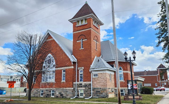 Traditional brick church with steeple, arched window, greenery, and a partly cloudy sky, evoking serenity and community.