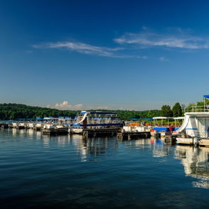 Serene lakeside scene with docks, boats, clear blue sky, lush greenery; evokes tranquility and summer nostalgia.