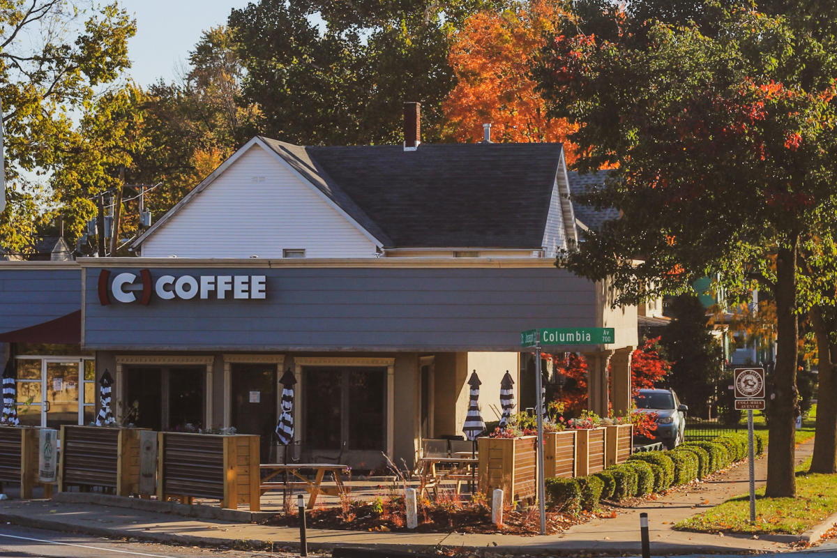 Cozy coffee shop on a fall street corner, surrounded by colorful leaves, with outdoor seating and a warm atmosphere.