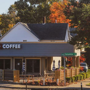 Cozy coffee shop on a fall street corner, surrounded by colorful leaves, with outdoor seating and a warm atmosphere.